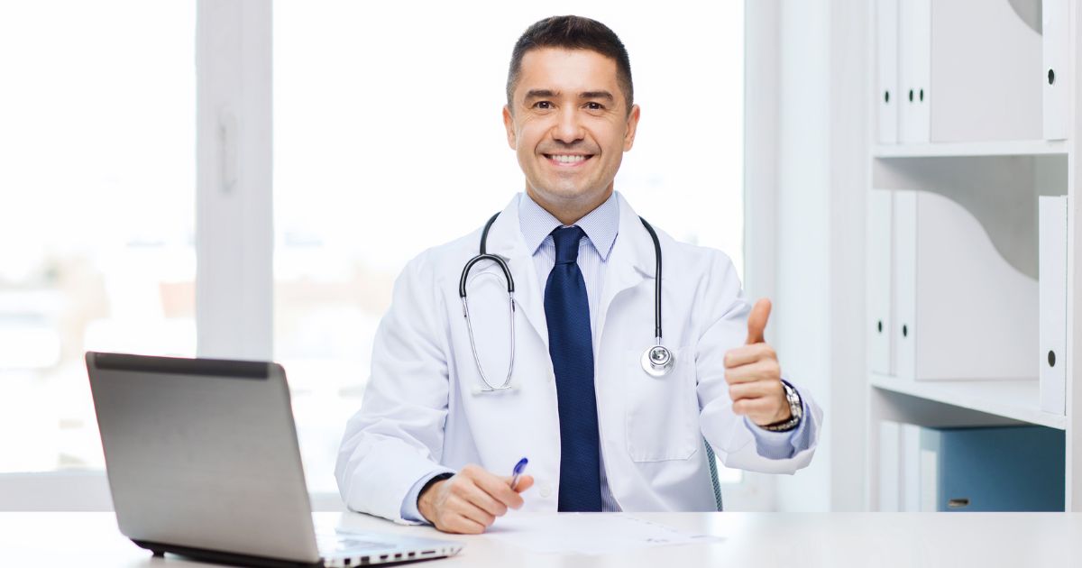 Doctor sitting at desk giving a thumbs up